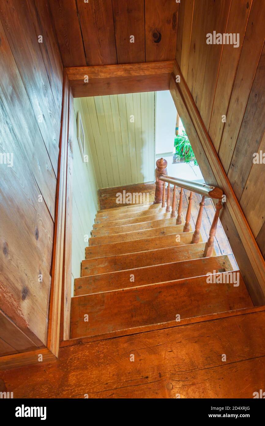 Looking down pinewood staircase with maple wood handrail and newel post inside an old 1841 cottage style fieldstone house. Stock Photo
