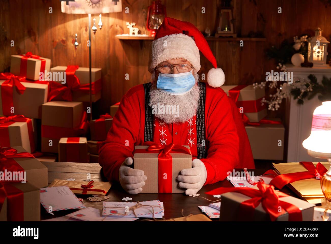 Santa wearing face mask holding Christmas gifts on xmas eve. Stock Photo