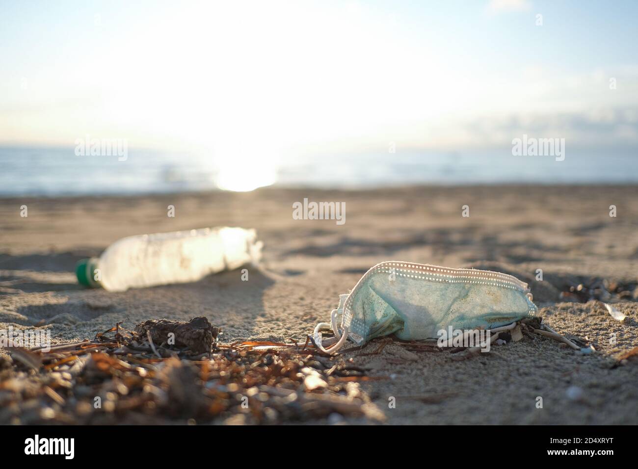 Medical face mask and plastic bottle discarded on dirty sea coast,covid19 pandemic disease pollution effects Stock Photo