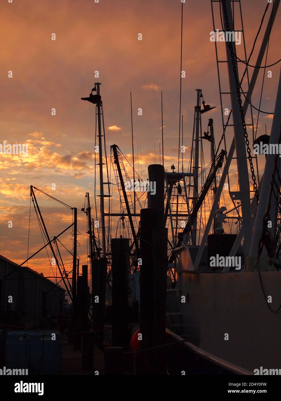 Fishing boat rigging in deep silhouette after sunset against a warm sky with red, yellow and orange clouds. Stock Photo