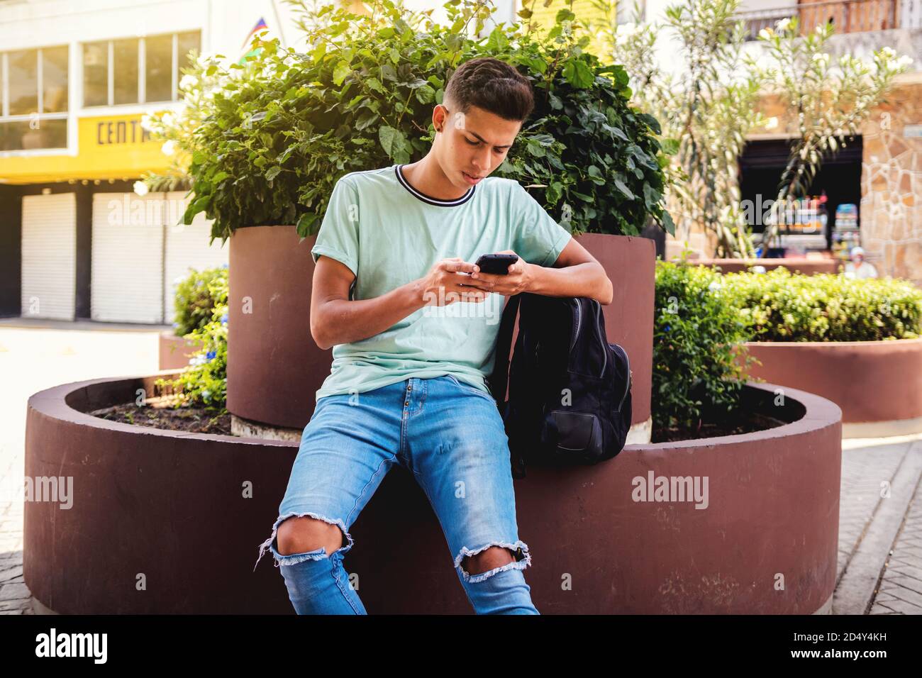Young Hispanic man sitting while texting through his phone Stock Photo