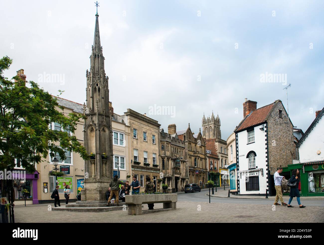Glastonbury Town Center and fully restored Market Cross. Crowds milling with two young men  fist bumping a greeting. Local stores visible. Stock Photo