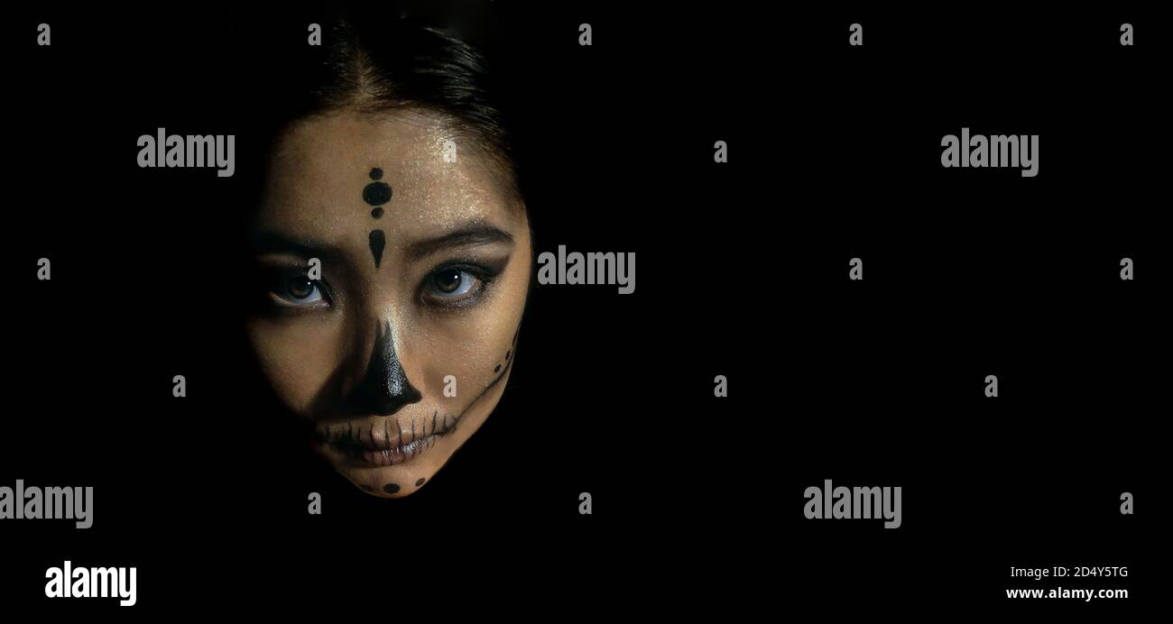 Young beautiful girl with skeleton makeup put her head on a pumpkin on a black isolated background. The concept of the Halloween celebration. Stock Photo