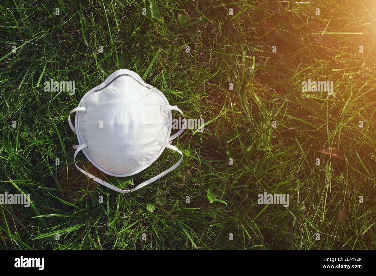 Medical mask on the green grass with sunlight spread. Ecology and protective concept. Coronavirus quarantine. World outbreak of coronavirus Stock Photo