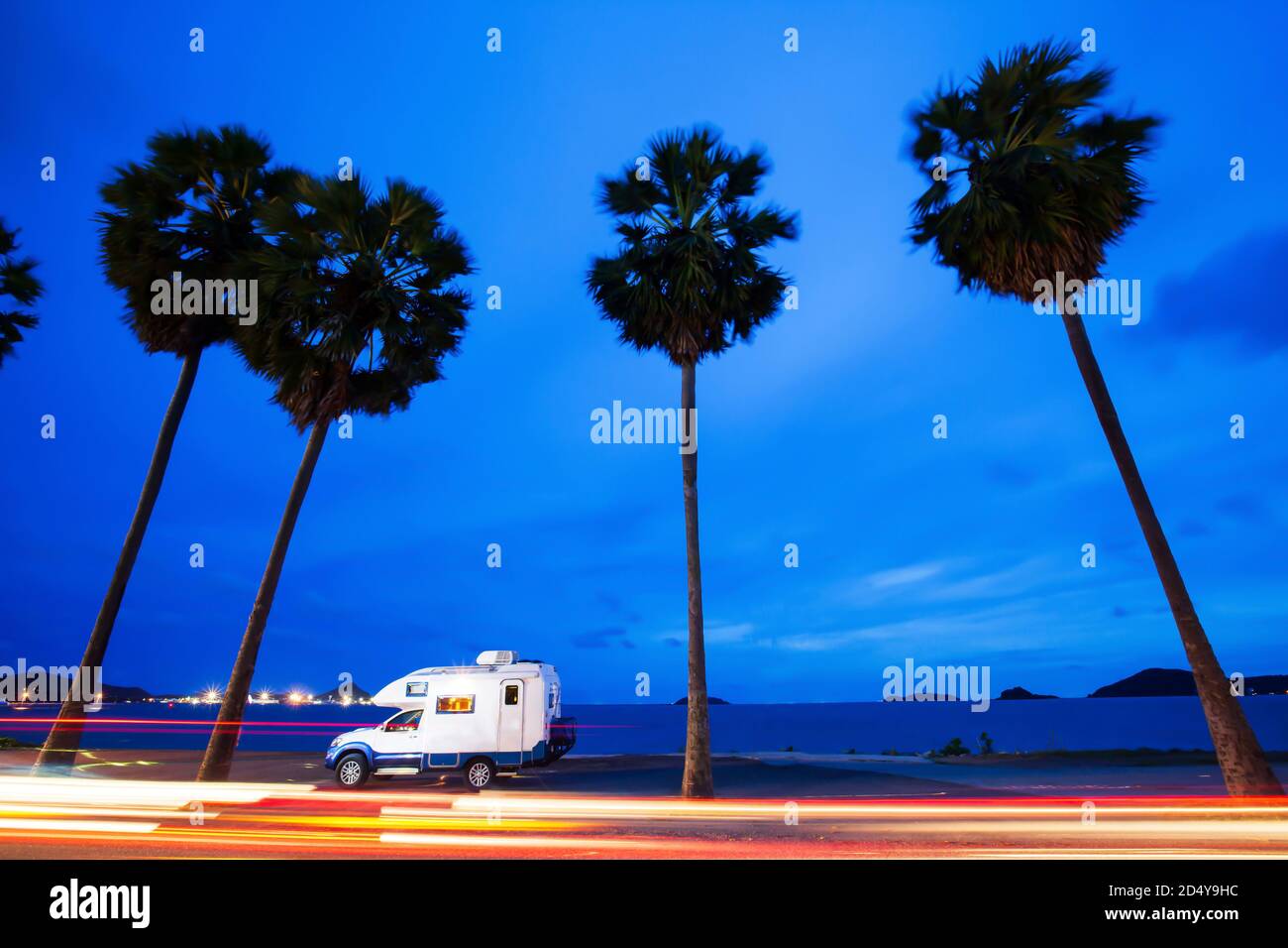Magical journey in motorhome on the road trip to palm beach in summer, bright lights trails against blue sky at twilight. Long exposure. Stock Photo
