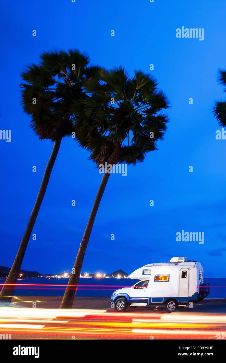 Magical journey in motorhome on the road trip to palm beach in summer, bright lights trails against blue sky at twilight. Long exposure. Stock Photo