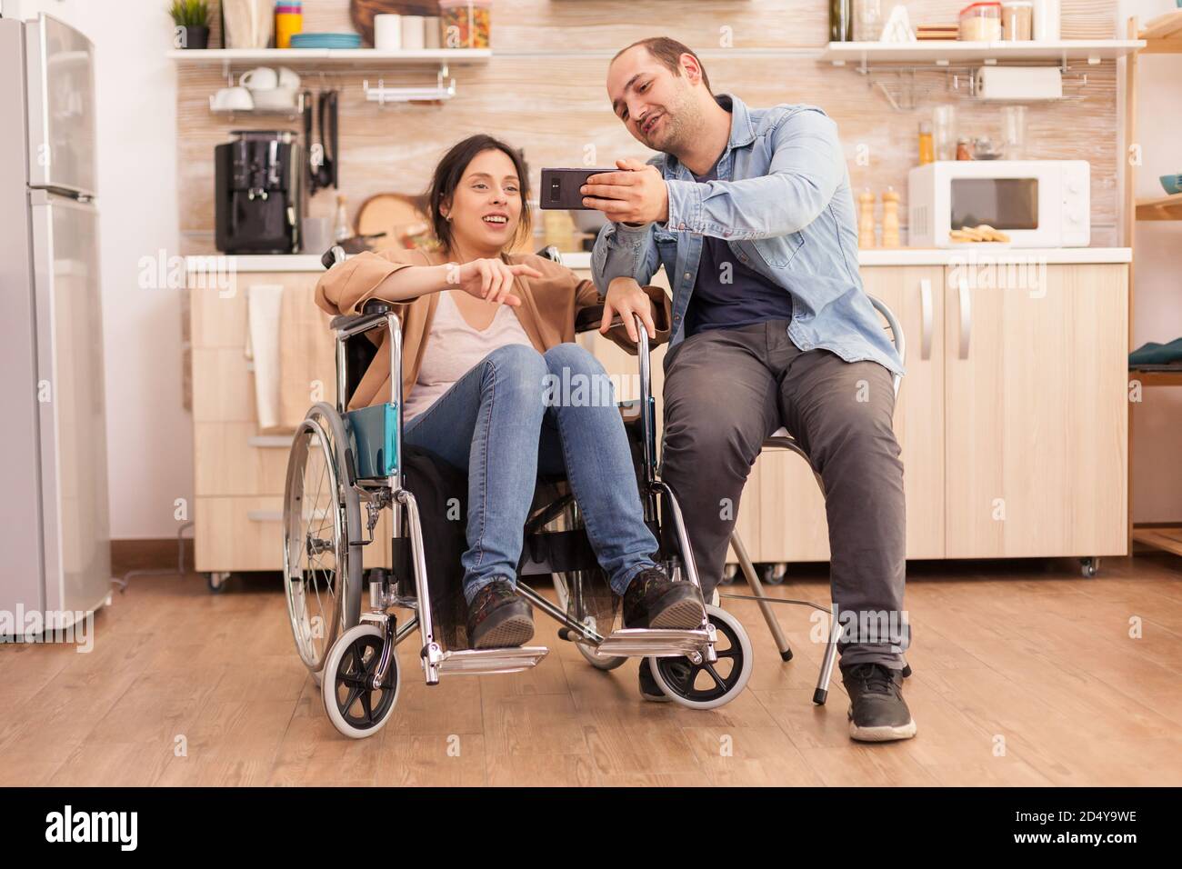 Cheerful disabled woman in wheelchair taking a selfie with husband in ...