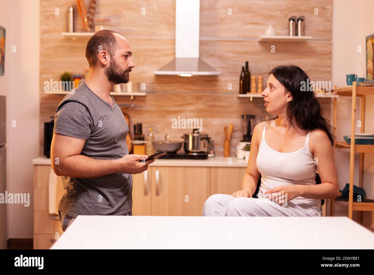 Angry husband confronting cheating wife about infidelity while holding her phone. Frustrated offended irritated accusing woman of infidelity arguing her. Stock Photo