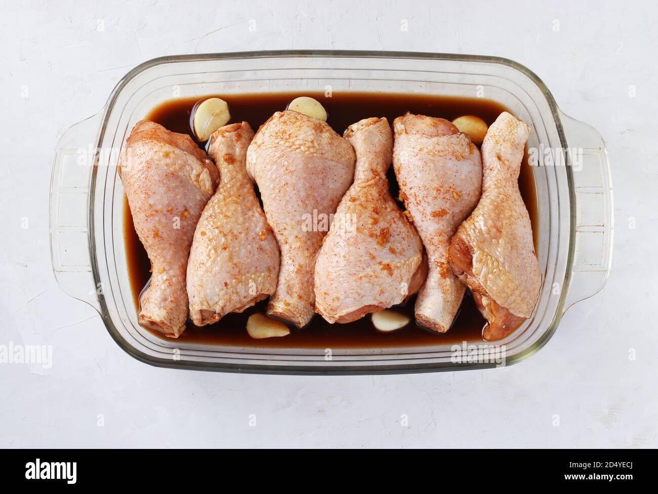 Raw chicken drumsticks in soy sauce with garlic in a mold before baking