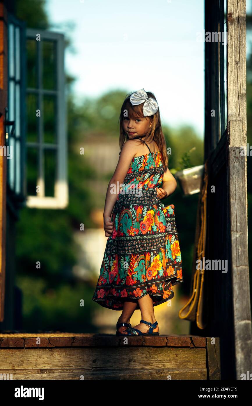 Little cute girl posing for the camera on the porch of a village house ...