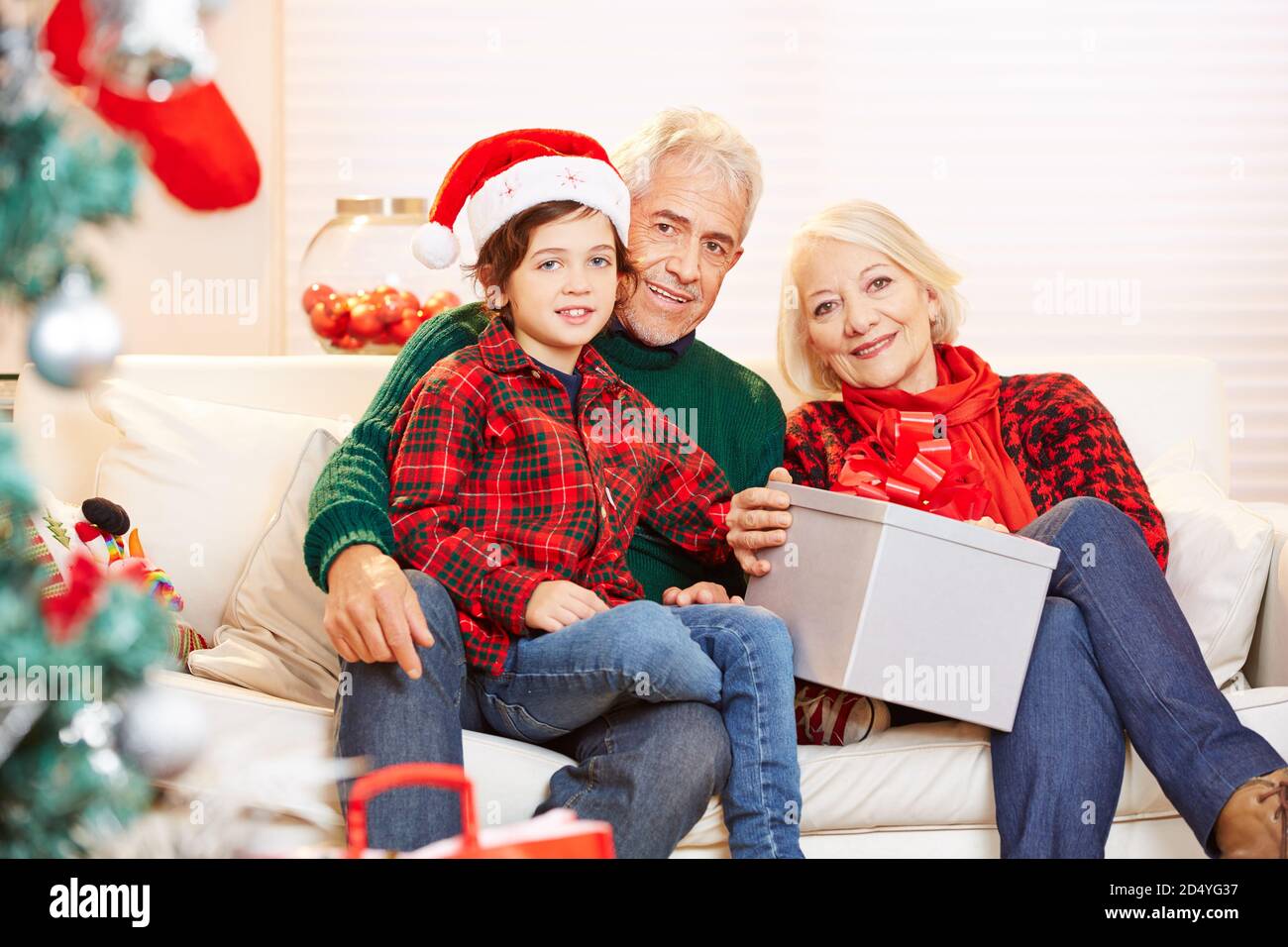 Grandson celebrates Christmas with his grandparents on the sofa next to the Christmas tree Stock Photo