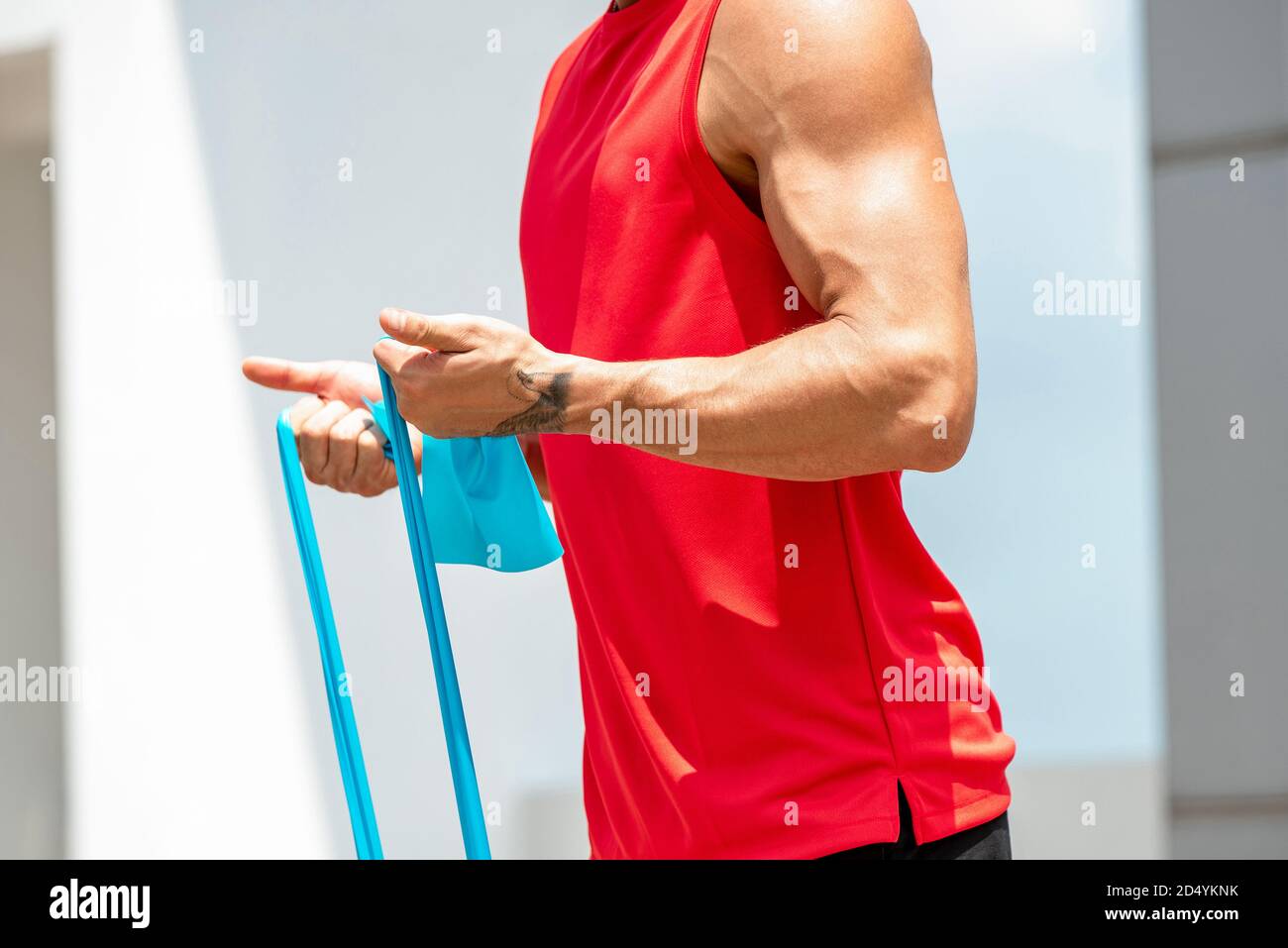 Faceless muscular athletic man doing bicep curl exercise with resistance band in the open air Stock Photo