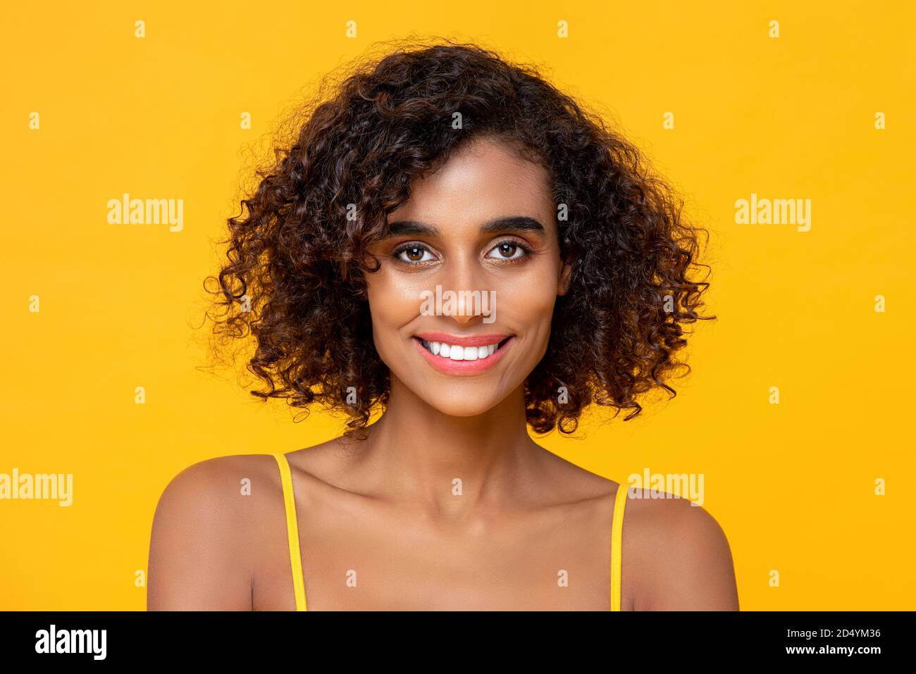 Happy smiling beautiful African American woman looking at camera isolated on colorful yellow background Stock Photo