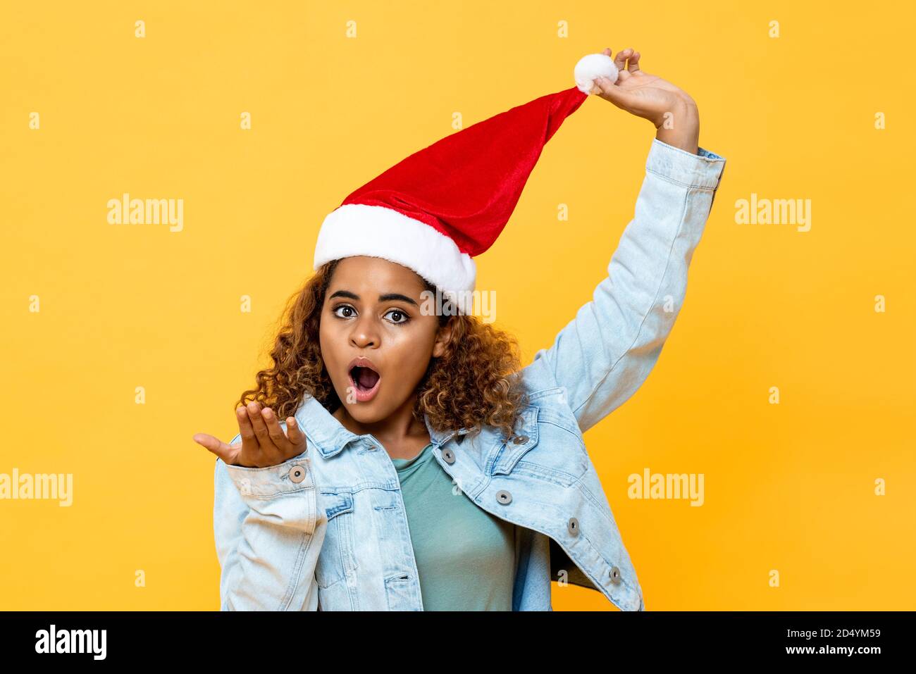 Funny surpried African American woman wearing Christmas hat with open palm gesture on yellow isolated background Stock Photo
