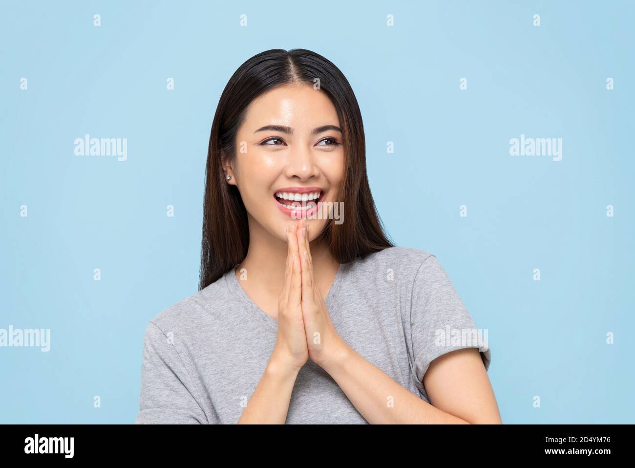 Smiling beautiful Asian woman doing Wai gesture for greeting or thank you isolated on light blue background Stock Photo