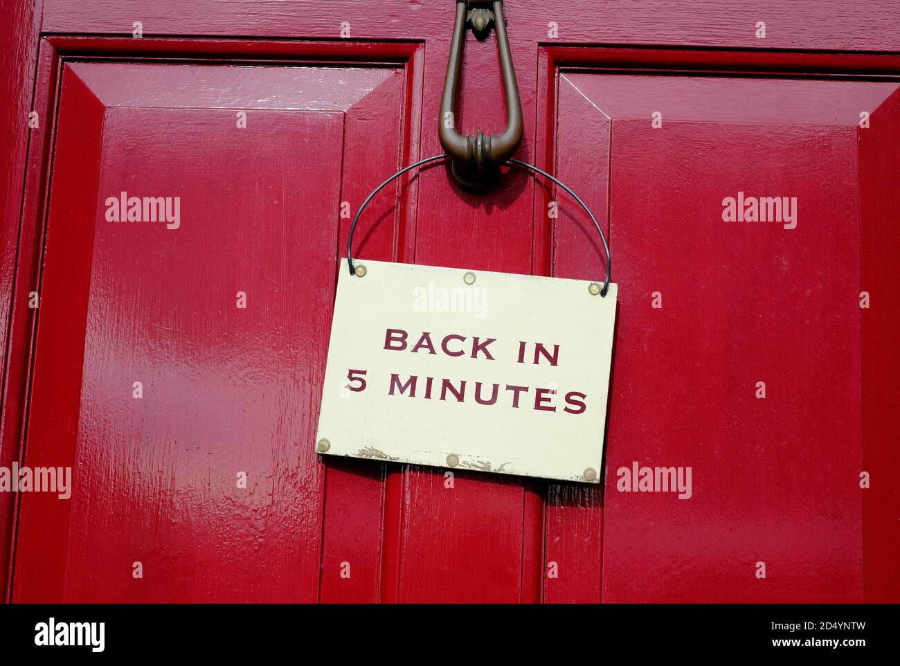 back in 5 minutes sign on red wooden door Stock Photo
