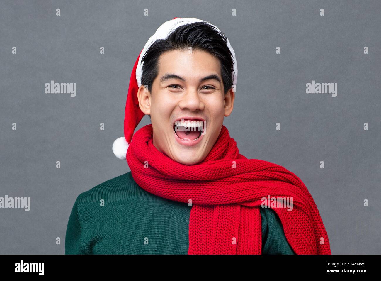 Happy surprised handsome Asian man wearing colorful red and green Christmas attire in studio gray background Stock Photo