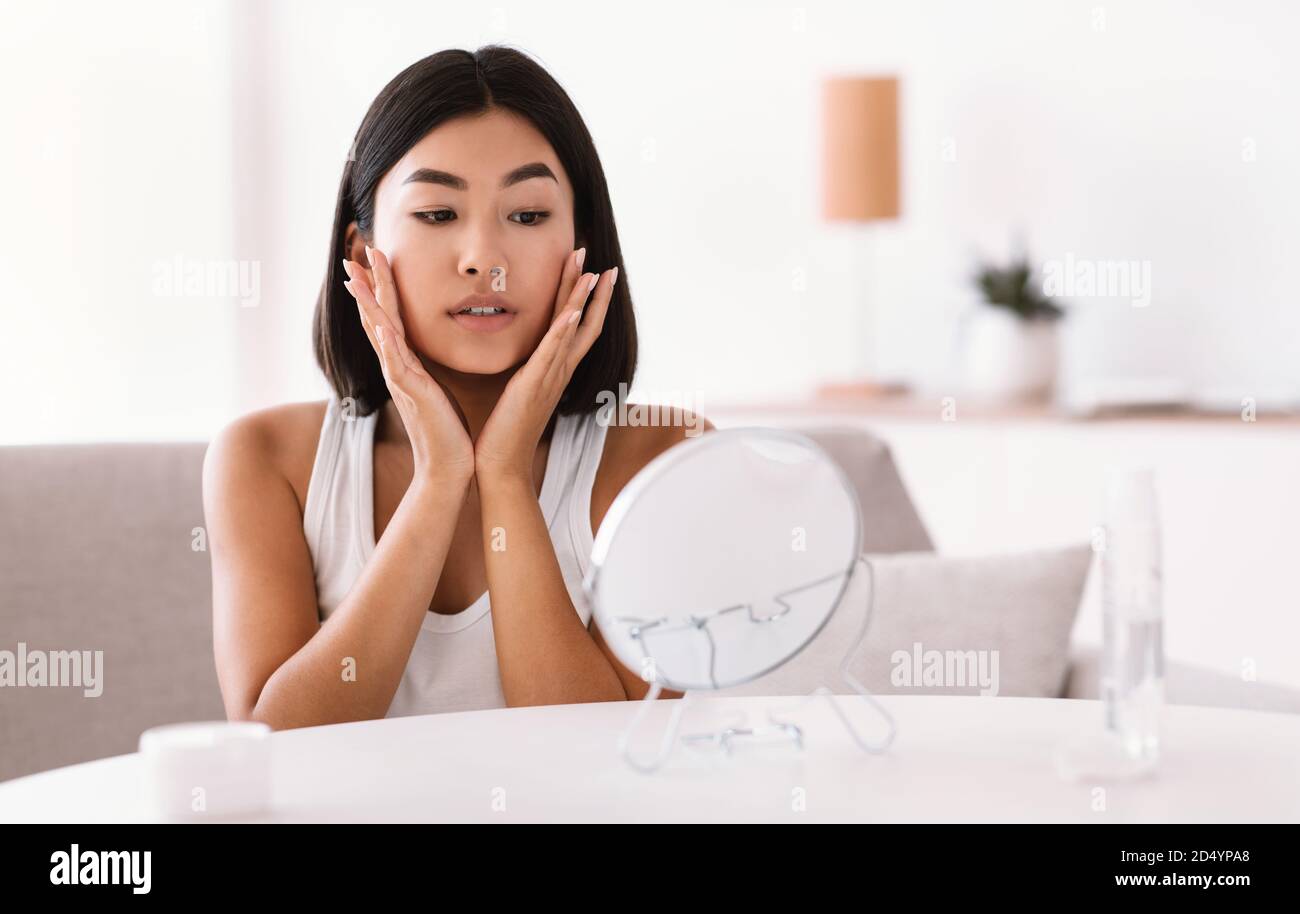 Young asian woman massaging her face looking in the mirror Stock Photo