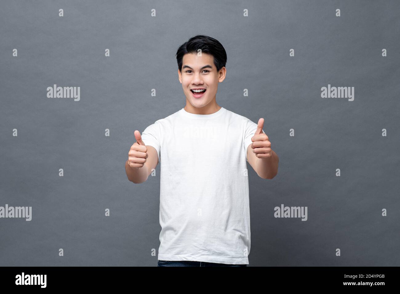 Handsome Asian man smiling and giving thumbs up on gray isolated ...
