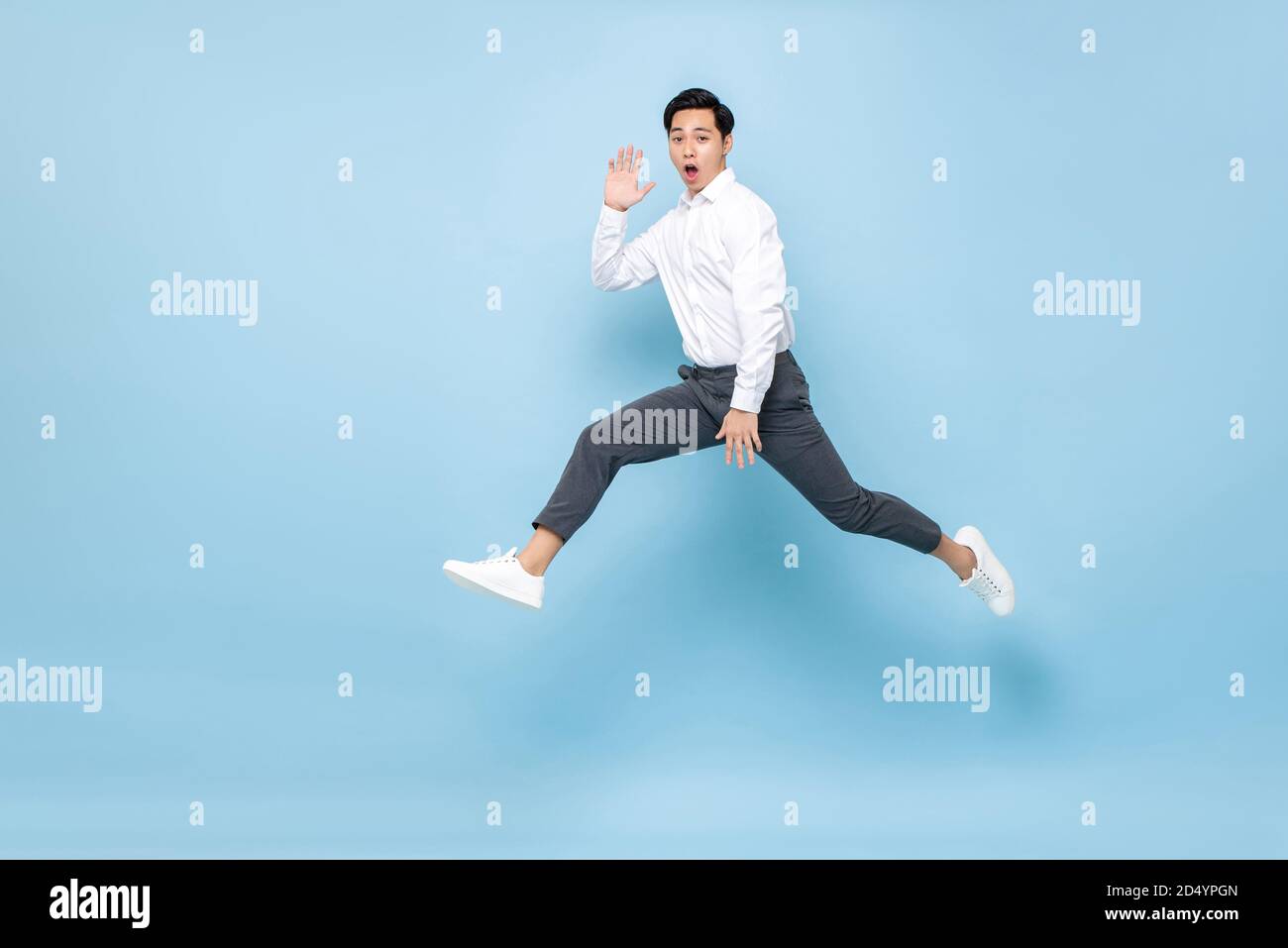 Fun energetic Asian man in semi formal clothes jumping in mid air isolated on light blue background Stock Photo