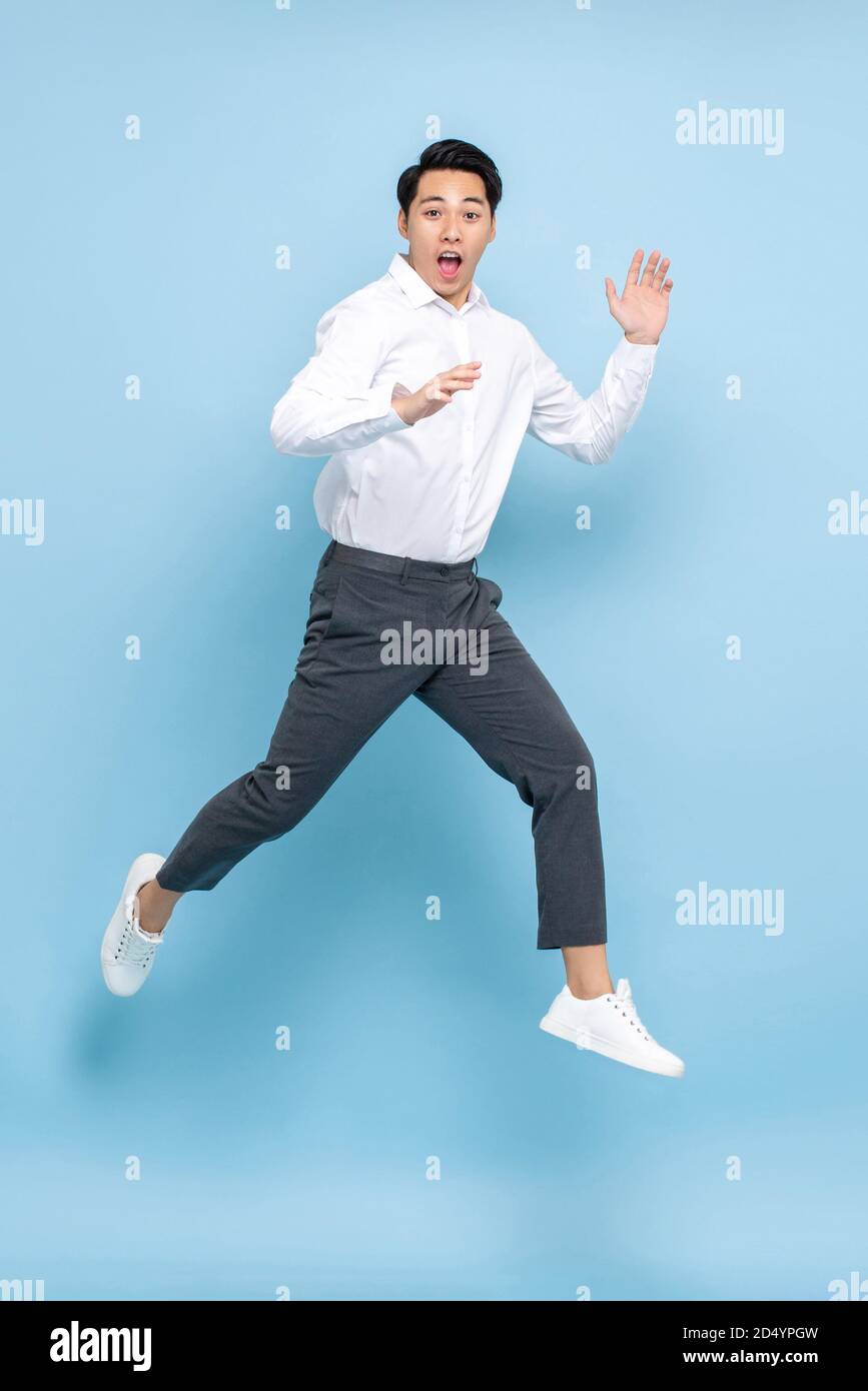 Energetic Asian man in semi formal clothes jumping in mid air isolated on light blue background Stock Photo