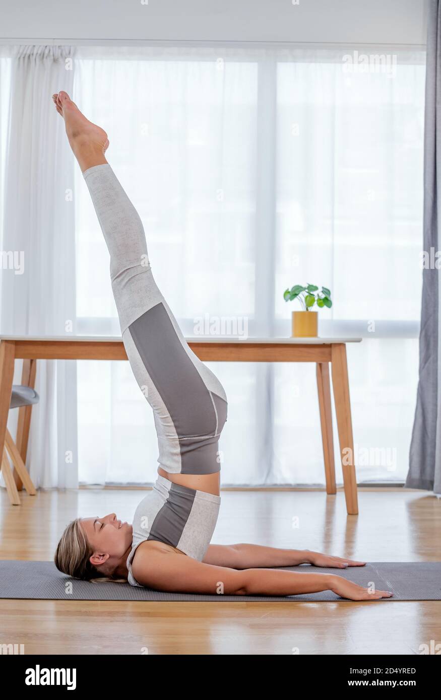 Beautiful active young woman doing shoulder stand on mat. Practicing