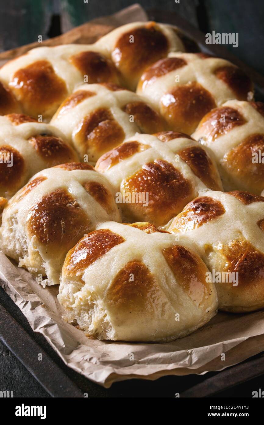 Homemade Easter traditional hot cross buns on oven tray with baking paper over dark wooden background. Close up Stock Photo