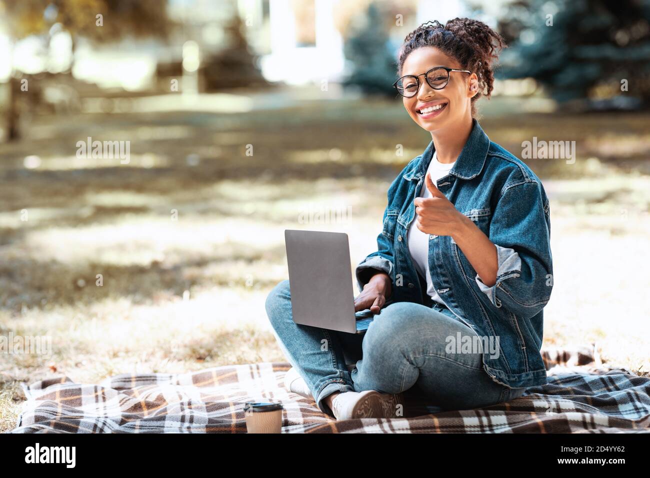 African Woman With Laptop Gesturing Thumbs Up Sitting In Park Stock ...