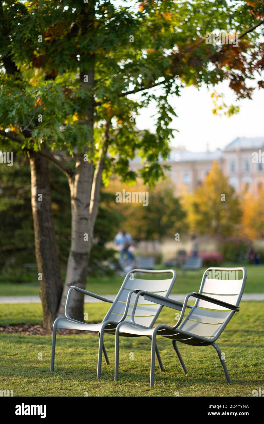 Green iron chairs on green lawn in empty public space. Autumn season. Stock Photo