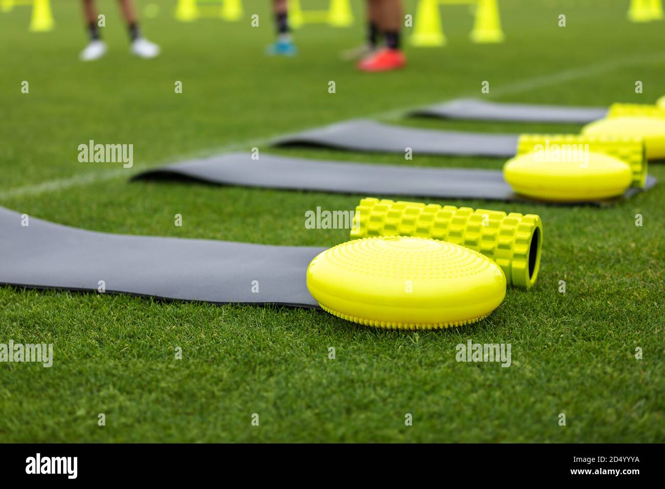 Training mat, goal roller and balance cushion. Sports training equipment on grass field. Young athletes and training cones in blurred background Stock Photo