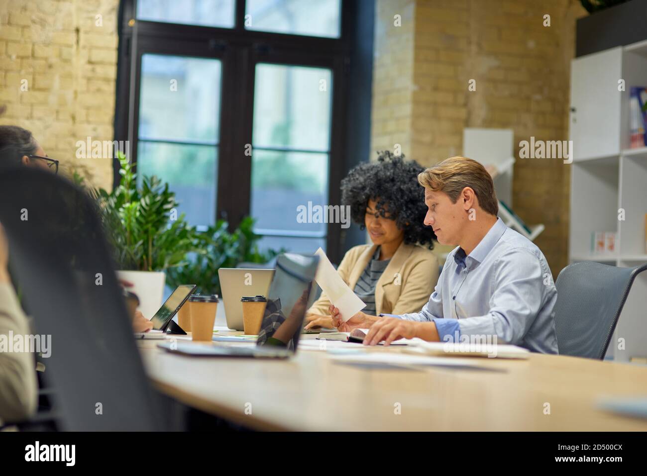 Business people working together. Two male and female coworkers looking at laptop screen and analyzing project results while sitting together at the table in the modern office or coworking space Stock Photo