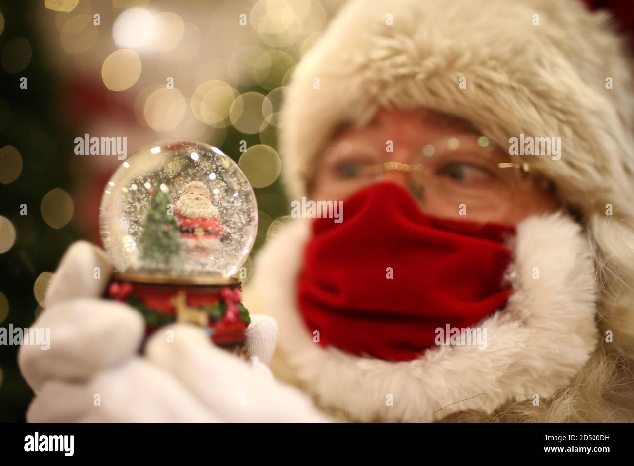 A man dressed as Father Christmas, wearing a protective face covering, looks at a snow globe at the launch of the Selfridges Christmas shop at the flagship store on Oxford Street, London. This year's theme has been unveiled as Once Upon A Christmas. Stock Photo
