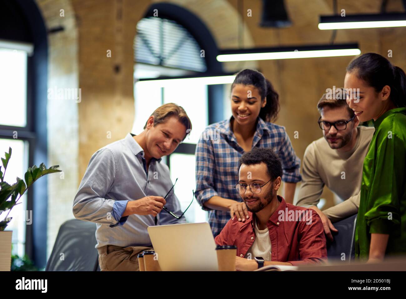 Good job. Group of happy multiracial business people looking at laptop screen, discussing project results and smiling while working together in the modern office or coworking space. Teamwork concept Stock Photo