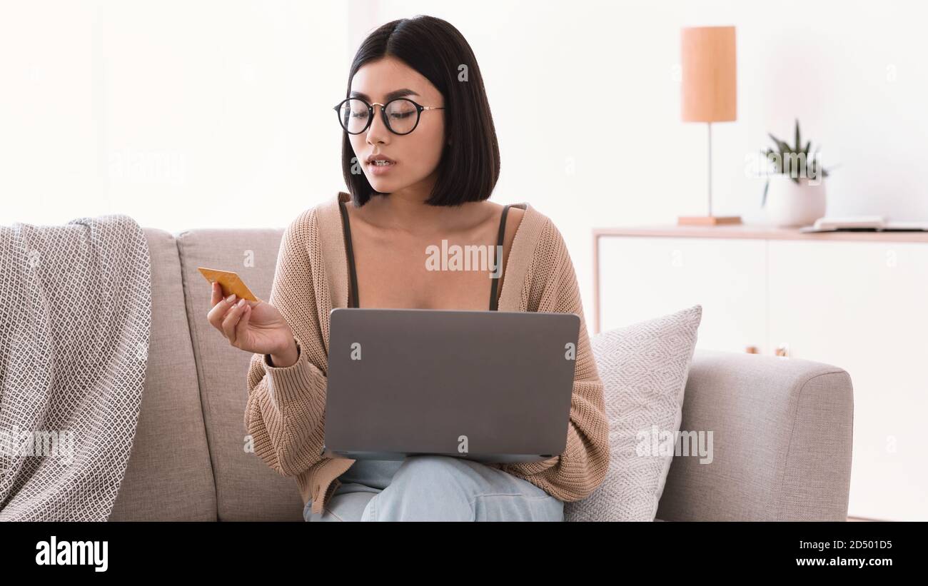 Young asian lady making purchases sitting with pc on couch Stock Photo