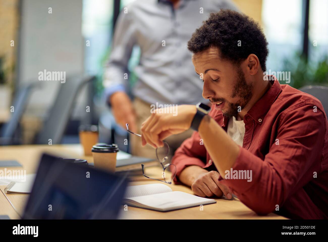 Business problems. Young frustrated and sad mixed race man sitting at desk and working in the modern office. Stressful work Stock Photo