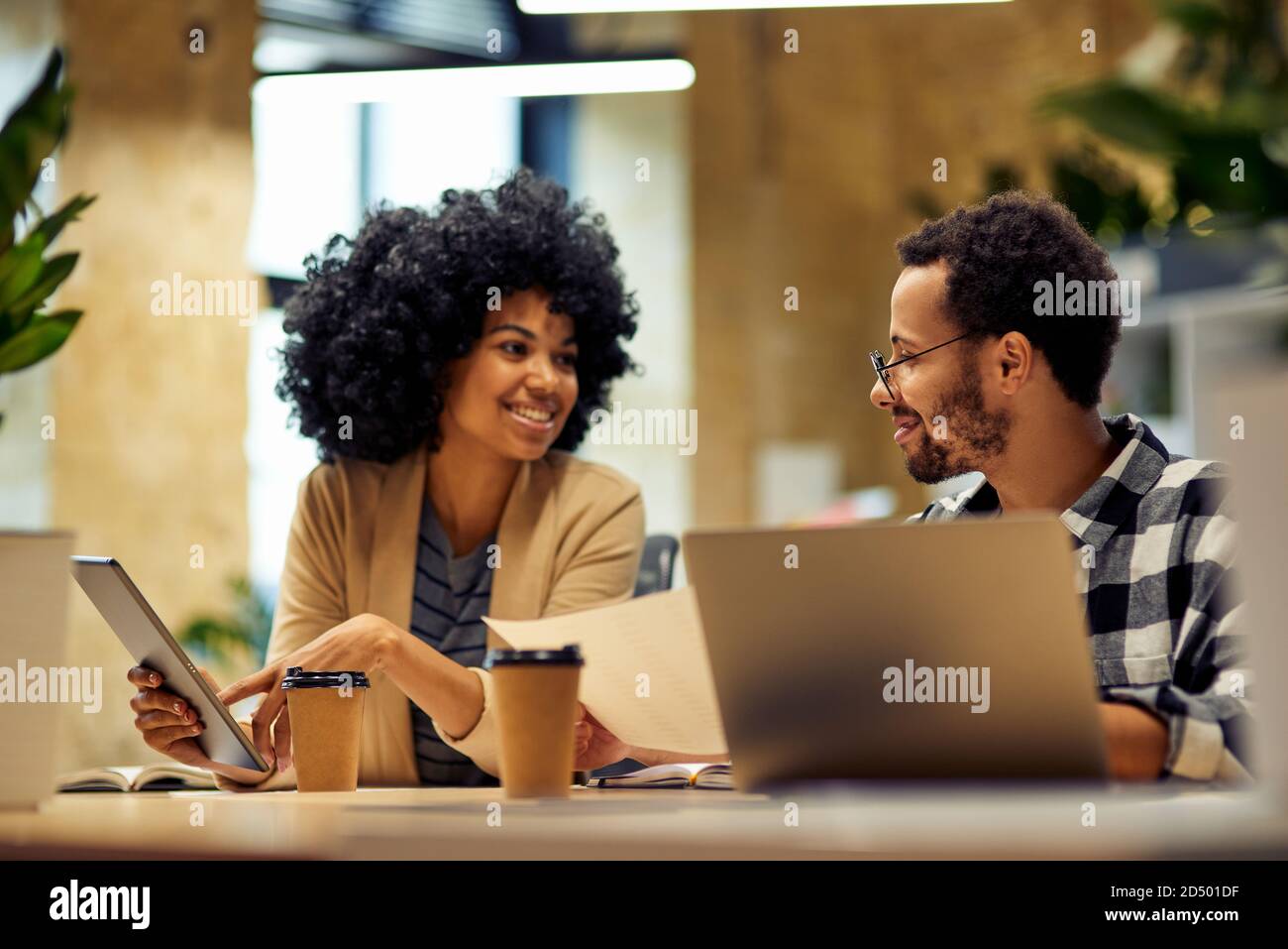 Sharing fresh ideas. Two young happy multiracial business people sitting at desk and communicating while working together in coworking space. Office life, teamwork and business Stock Photo