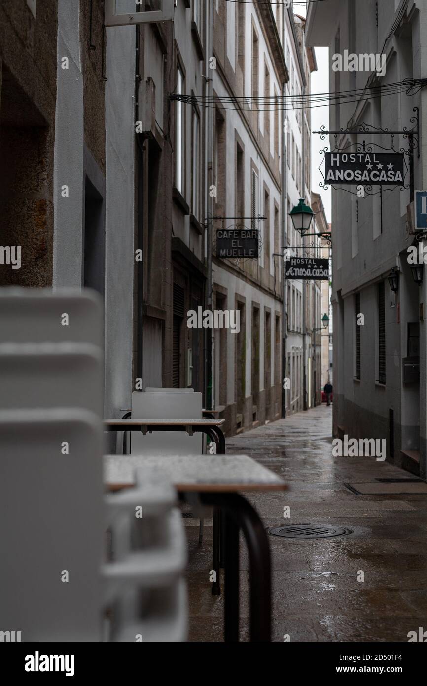 Santiago de Compostela, Galicia, Spain - 09/26/2020: Stacked plastic chairs and tables in a narrow empty hostel street with a closed cafe. Stock Photo