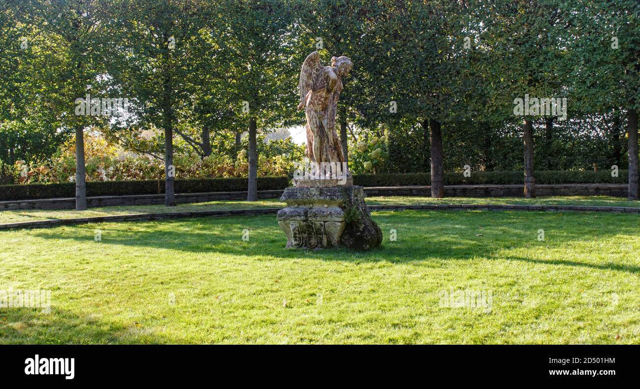 antique angel statue on a green lawn surrounded by trimmed linden trees Stock Photo