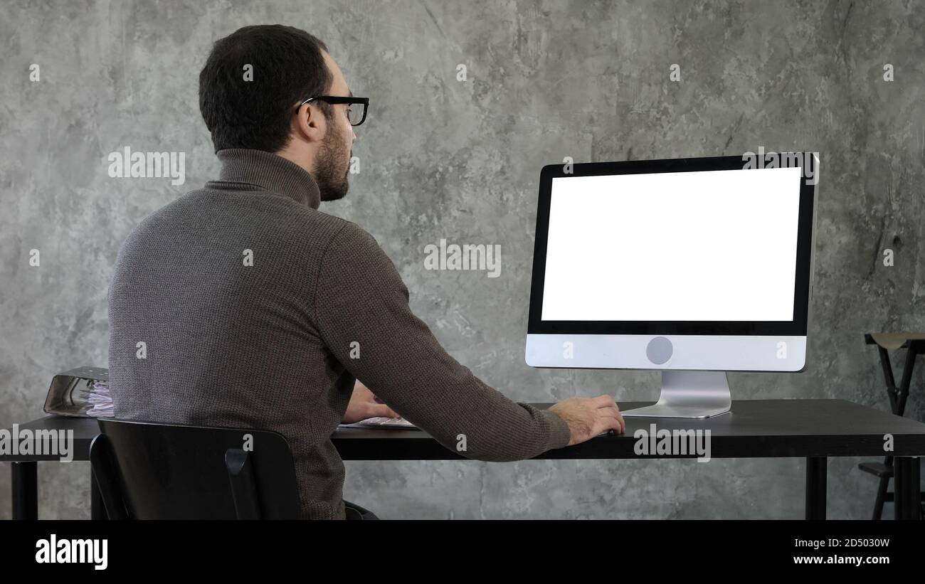 Bearded young businessman woking on computer. White Display. Stock Photo