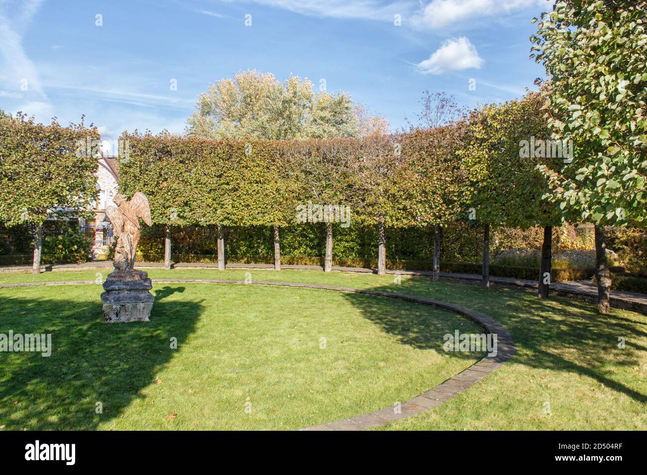 antique angel statue on a green lawn surrounded by trimmed linden trees Stock Photo