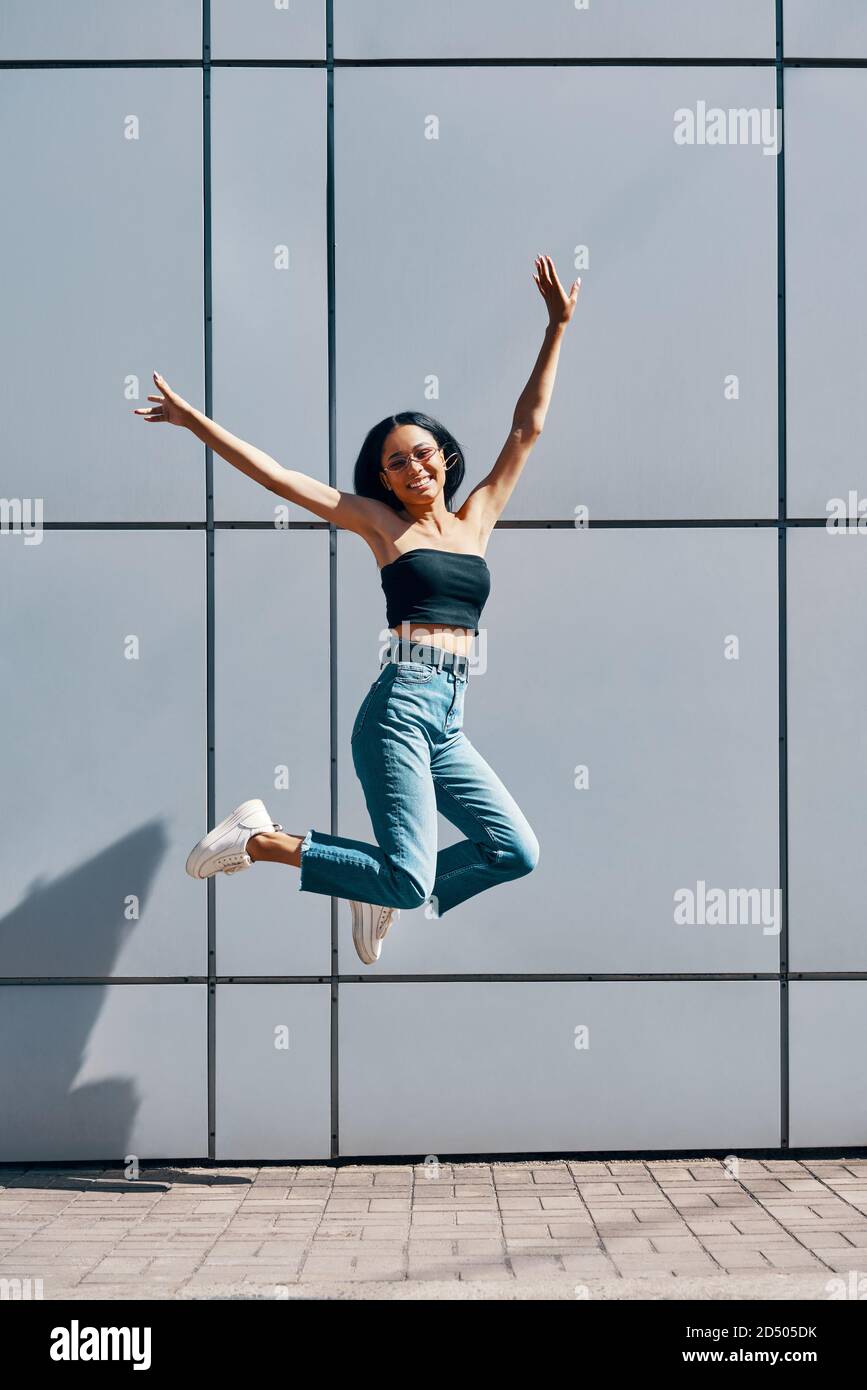 Portrait of cheerful positive black girl jumping in the air on wall ...