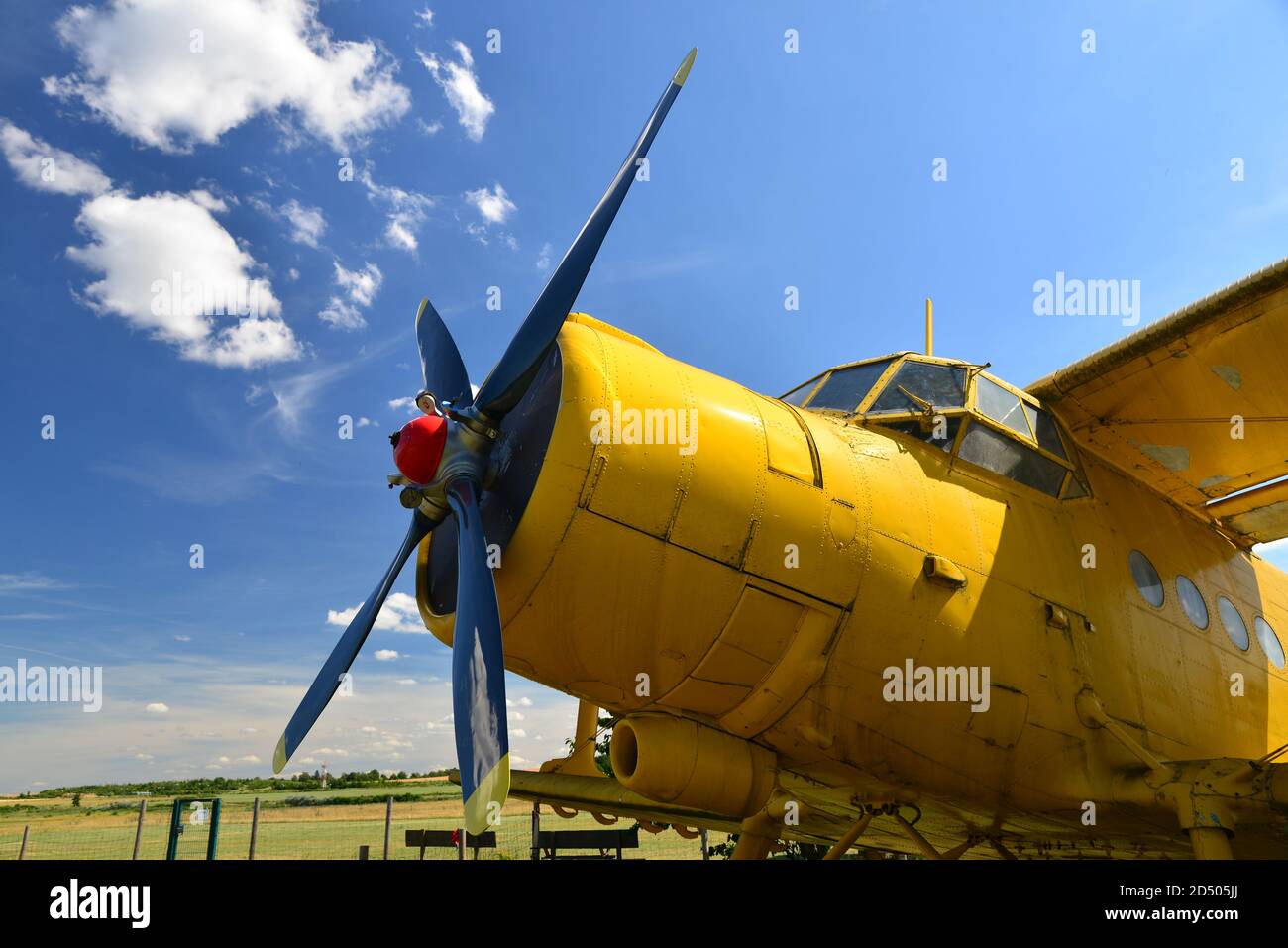 Close-up view of an old yellow plane. Isolated yellow bi plane on grassy meadow under blue sky with dynamic clouds. Aircraft at a grassy airfield. Stock Photo