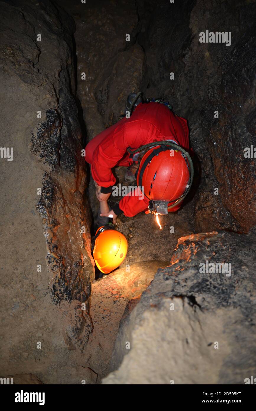 Caver in overalls in a narrow cave. Rescue from a narrow place of a stone cave. Historic mining light. Cave rescue. Spelunking, extreme sport. Stock Photo