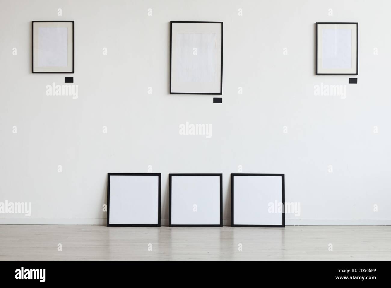 Background image of empty black frames hanging on white wall at art