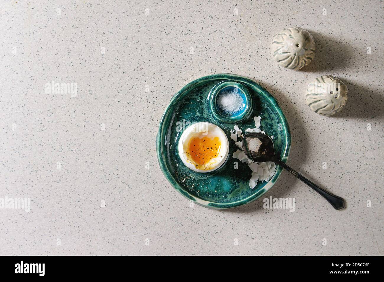 Breakfast with soft boiled egg, served in green ceramic egg cup with salt and pepper over grey spotted table. Stock Photo
