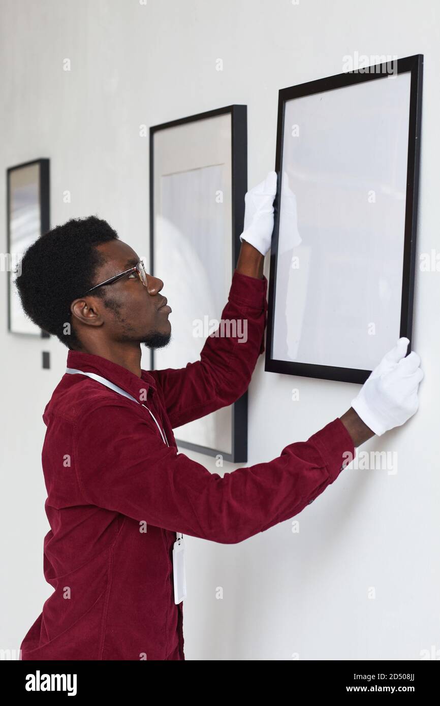 Vertical side view at AfricanAmerican man hanging frames on wall while