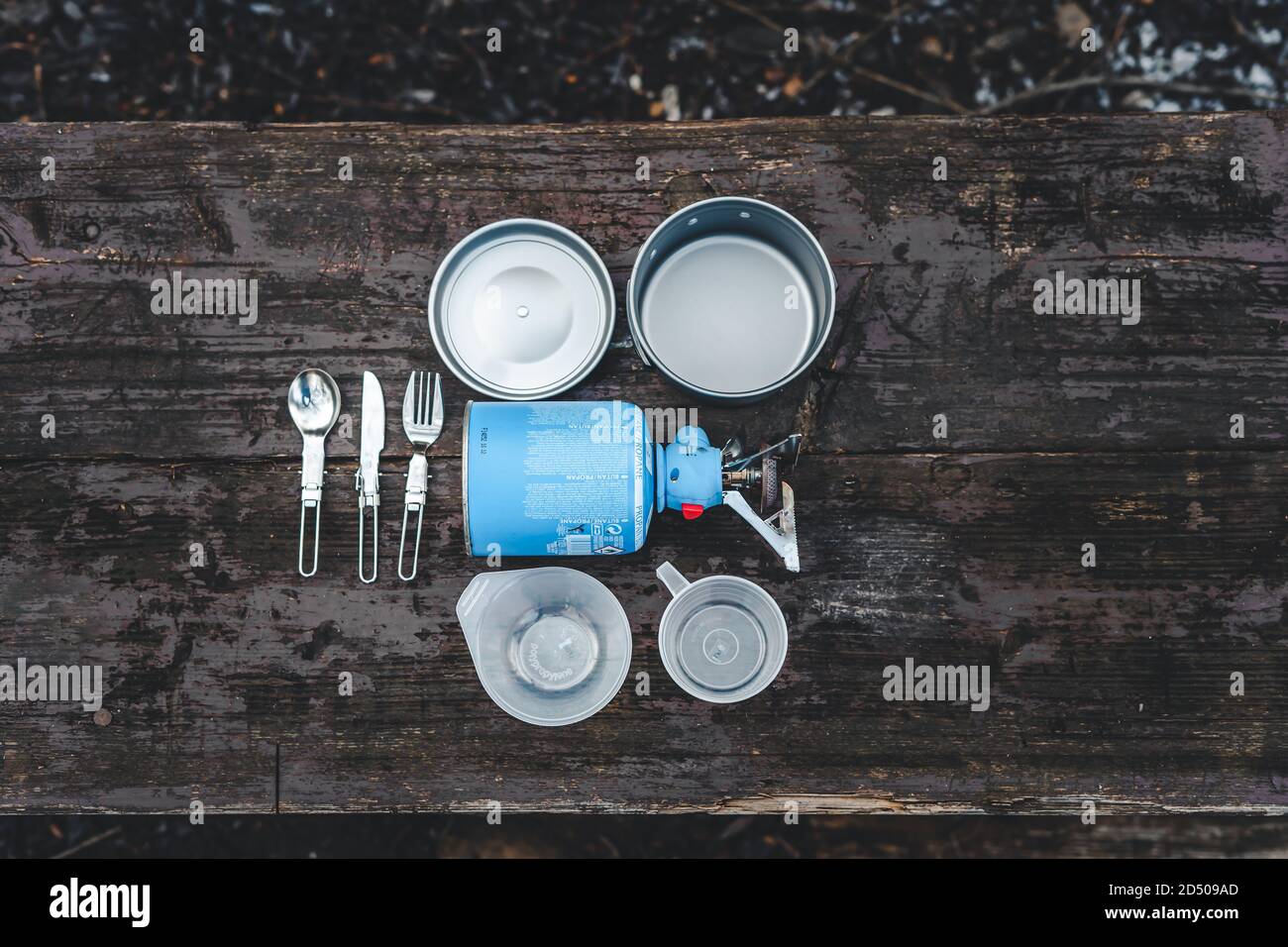Cooking camping, tourism and travel equipment set with gas stove, pot and cutlery on wooden table. Stock Photo