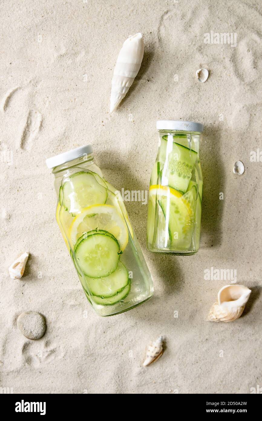 Summer drinks theme. Two glass bottles with lemon and cucumber infusion sassy water on white sand as background. Flat lay, space Stock Photo