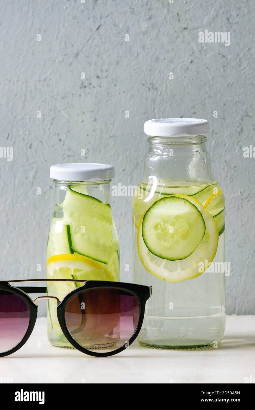Summer drinks theme. Two glass bottles with lemon and cucumber infusion sassy water and sunglasses on white marble table with concrete wall at backgro Stock Photo