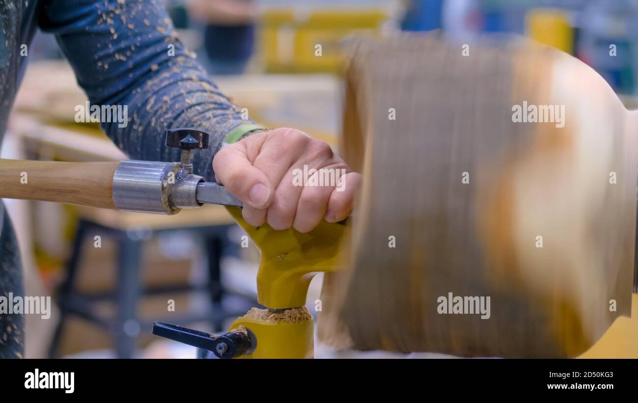 Professional man carpenter holding skew chisel, shaping piece of wood
